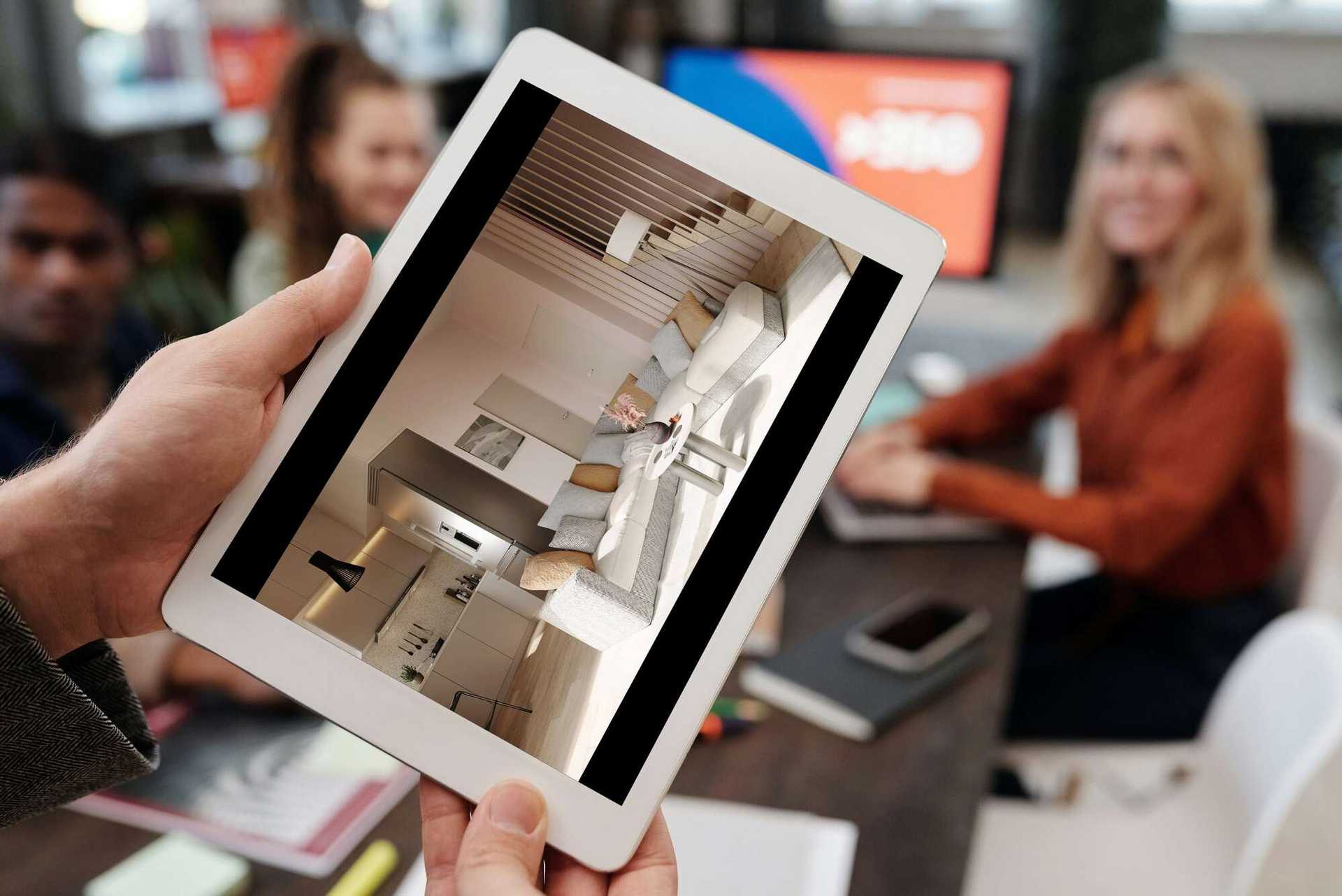 Ręce trzymają tablet, na którym wyświetlona jest wizualizacja wnętrza 3D nowoczesnego salonu z aneksem kuchennym i jadalnią.