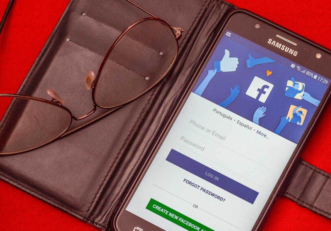 Smartfon z otwartą aplikacją Facebook, umieszczony w skórzanym etui obok okularów