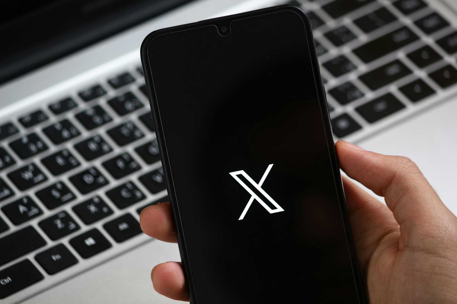 Ręka trzymająca smartfon z logo platformy X (dawniej Twitter) na czarnym ekranie