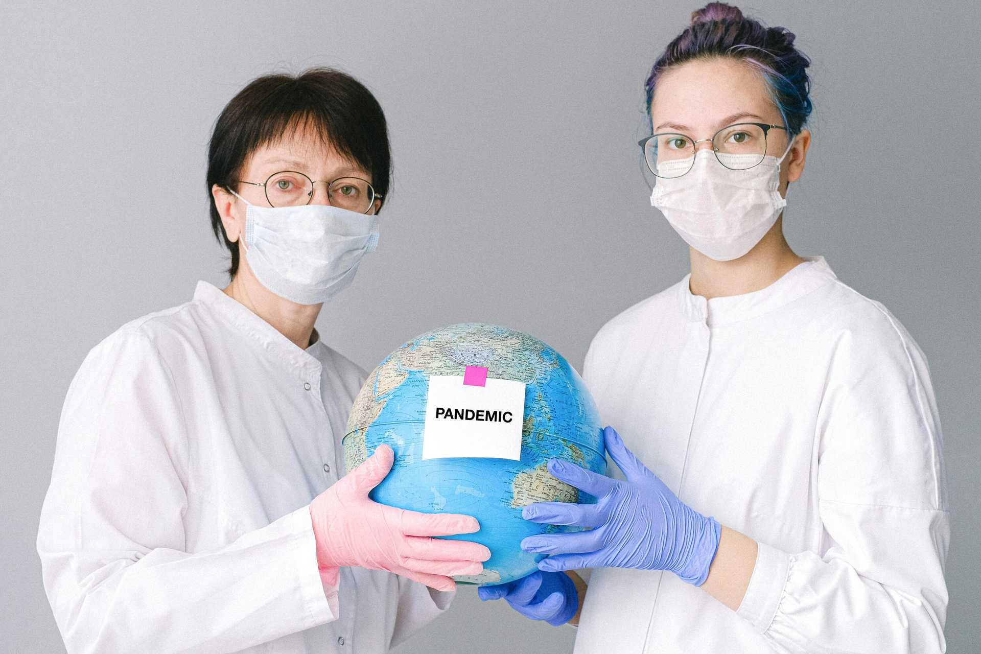 Dwie osoby w maseczkach ochronnych trzymające globus z napisem „Pandemic”