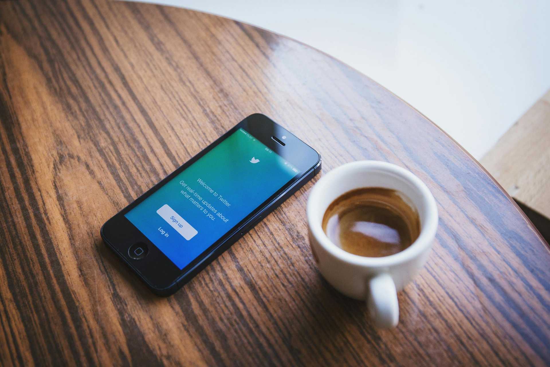 Smartfon z otwartą aplikacją na ekranie i filiżanka espresso na drewnianym stole